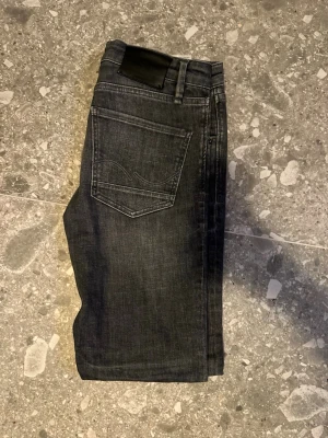 Mörkgrå straight leg jeans från Jack and jones - Snygga mörkgrå jeans från Jack and jones med klassisk femficksdesign och diskreta sömmar på bakfickan. Jeansen har en slim passform och är tillverkade i mjuk bomull med en liten stretch för extra komfort. Perfekta för dig som gillar en stilren look.