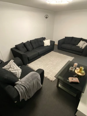 Mörkgrå soffgrupp med kuddar - Säljer en stilren soffgrupp i mörkgrått tyg med tre matchande soffor. Sofforna har raka former, breda armstöd och lösa ryggkuddar. Medföljer flera dekorativa vita kuddar. Perfekt för vardagsrum eller lounge.