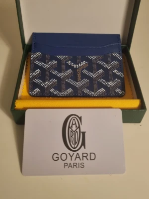 Blå korthållare från G4yard - Snygg blå korthållare från G4yard med det klassiska vita och gråa G4yard-mönstret. Tillverkad i läder och canvas, har flera fack för kort och är perfekt för dig som vill ha en stilren och exklusiv accessoar. Levereras med originalask och tygpåse.