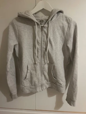 Ljusgrå zip hoodie med huva - En enkel och stilren ljusgrå hoodie med dragkedja framtill och två fickor. Hoodien har justerbar huva med snören och ribbade muddar vid ärmar och nederkant. Perfekt för en avslappnad look och passar till det mesta. Skriv vid frågor 💕💕