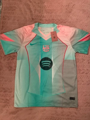 Barça matchtröja turkos/rosa Nike - Säljer en FC Barcelona matchtröja från Nike i turkos och rosa med vita och röda detaljer. Tröjan har klubbmärke och Spotify-logga på bröstet samt rund halsringning. Tillverkad i lätt och ventilerande funktionsmaterial, perfekt för fotbollsträning.