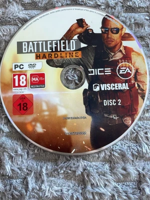 Battlefield Hardline PC Disc 2 - Battlefield Hardline Disc 2 till PC, originalskiva från EA och Visceral. Skivan är rund och gjord av plast med tryckt motiv i orange, svart och vitt. Märkt med åldersgräns 18+ och logotyper för DICE och Visceral. Perfekt för dig som gillar actionspel. Den är värd runt 250-300 kr.