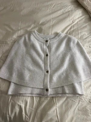 Ljusgrå stickad cape från Kappahl - Säljer en beige/vit stickad cape från Kappahl. Capen är gjord i mjukt material som är super bekväm att ha på sig. Storlek 158-164. Har andvänt 2-3 gånger så den är i superfint skick, säljer för att den ej kommer till andvänding💕
