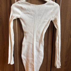 Vit ribbad långärmad klänning - Säljer en vit, ribbad klänning med lång ärm och djup uringning i ryggen. Klänningen har en kroppsnära passform och är tillverkad i ett stretchigt material som formar sig snyggt efter kroppen. Perfekt för dig som gillar en enkel men stilren look.Aldrig använd, väldigt strechig så passar även folk i strl xs och s skulle jag säga