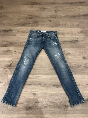 Blå slitna jeans från Replay - Säljer ett par blå jeans från Replay med slitningar och distressed detaljer på både fram- och baksida. Klassisk femficksmodell med dragkedja och knapp. Jeansen har en bra passform och cool tvätt som ger den perfekta ”Grisch” stilen många söker. Priset kan eventuellt diskuteras! 