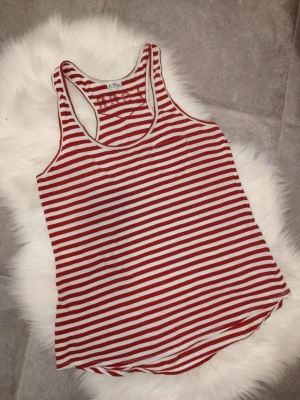 Jättefin rödvit randig Levi's linnetopp/tanktopp, storlek S - Snygg Levi's randig linnetopp i rött och vitt med brottarrygg och liten bröstficka. Perfekt för varma dagar och enkel att matcha med jeans eller shorts. Tillverkad i mjuk bomull för en skön känsla. Är i fint använt skick. Storlek S