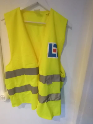 Gul reflexväst med tryck - Gul reflexväst från Reflexsafe med två breda reflexband runt midjan och tryckt logga på bröstet. Västen är tillverkad i 100% polyester och har en öppen passform som passar storlek M till XXL. Perfekt för synlighet utomhus.