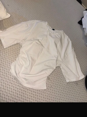 Vit oversized t-shirt - En enkel vit oversized t-shirt med rund hals och korta ärmar. T-shirten har en loose passform och är tillverkad i mjuk bomull, perfekt för en avslappnad stil.