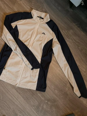 Vit & marinblå vindjacka J.Lindeberg - J.Lindeberg vind jacka i vit o marinblå, supersnygg men kommer ej till användning, helt ny oanvänd endast att jag tagit av prislappen. 