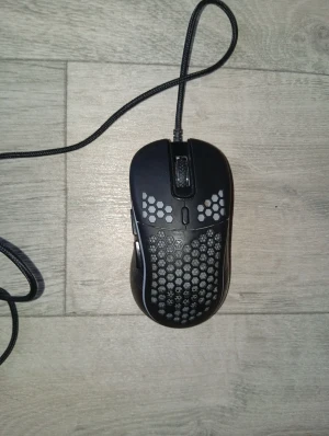 SR7 Gamingmus med sladd - Säljer en svart SR7 gamingmus med sladd och honeycomb-design för extra ventilation. Musen har ergonomisk form, flera knappar och en lätt konstruktion som passar perfekt för gaming. Materialet är plast med matt finish och flätad kabel för hållbarhet.