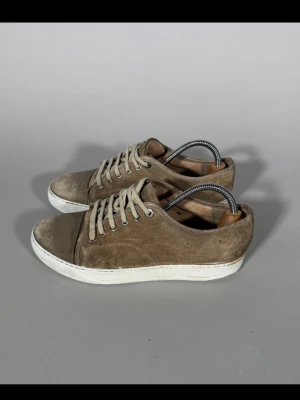 Lanvin skor - Snygga sneakers i beige mocka med vita snören och vit sula. Klassisk låg modell med rund tå och diskret design som passar till det mesta. Skorna har metallhål för snörningen och en stilren look.
