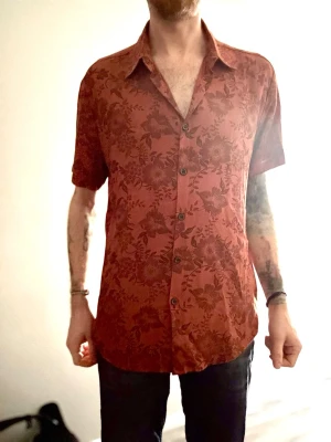 Orange blommig skjorta med kort ärm - Säljer en orange skjorta med blommigt mönster och korta ärmar. Skjortan har klassisk krage, knappar framtill och en relaxed passform. Perfekt för dig som vill sticka ut lite extra med en snygg och unik look. Nypris 550:-. Använd en gång. Stor passform så passar även för M.