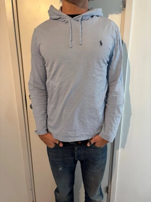 Ralph Lauren hoodie   - Snygg ljusblå hoodie från Ralph Lauren med klassisk huva och dragsko. Tillverkad i mjukt bomullsmaterial och har den ikoniska lilla loggan broderad på bröstet. Perfekt för en avslappnad och stilren look. Defekter på bild 