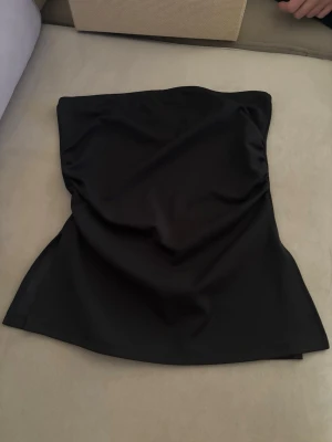 Svart axelbandslös tubtopp - Snygg svart tubtopp i stretchigt material. Axelbandslös design som sitter tight mot kroppen. Helt oanvänd med prislapp kvar! Storlek S! Skriv för fler bilder eller frågor💖