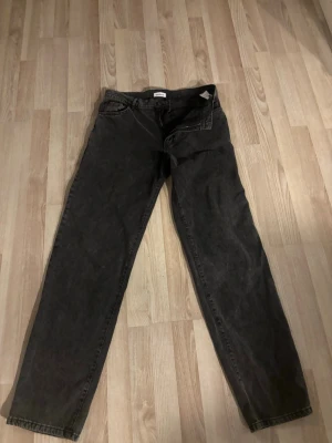 Mörkgrå jeans från Woodbird - Säljer ett par mörkgrå jeans från Woodbird i rak modell. Jeansen har klassisk femficksdesign och är tillverkade i ett mjukt denimtyg. Perfekta för dig som gillar en clean och avslappnad stil.