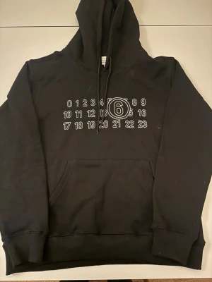 Maison Margiela Hoodie - Svart hoodie från Maison Margiela med tryck. Storlek 46, sitter som S/M. Väldigt bra skick, knappt använd. Tveka inte att skriva vid minsta fundering! 