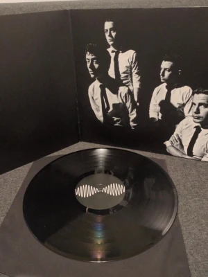 Vinylskiva Arctic Monkeys AM - Säljer en svart vinylskiva av Arctic Monkeys, albumet AM. Omslaget är svart med vit ljudvåg och insidan har ett svartvitt foto på bandet i kostym. Perfekt för dig som gillar indie rock och vill ha snygg samlarpryl till skivsamlingen.