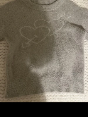 Tröja med hjärtan & pil igenom från Yamz. - Mysig tröja med fluffig textur och ett vitt hjärtmotiv framtill. Tröjan har rund halsringning och långa ärmar, tröjan är knappast använd. Nypris ca 600/700kr