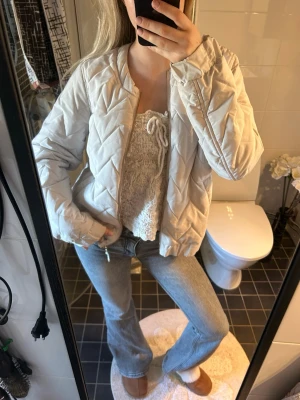 Beige quiltad bomberjacka - Snygg beige bomberjacka med quiltat mönster och dragkedja framtill. Jackan har en avslappnad passform och ribbade muddar vid ärmslut och nederkant. Perfekt för dig som vill ha en trendig och bekväm jacka till vardagslooken.