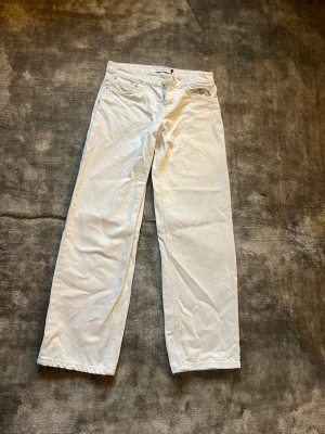 Vita wide leg jeans lowwaist - Säljer ett par vita jeans med wide leg passform och klassisk femficksdesign. Jeansen har låg midja och stängs med knapp och dragkedja. Perfekta för en clean och stilren look. Obs hål vid fickan se bild och någon liten fläck vid knät inte testat tvätta men syns knappt när man har dem på sig🥰
