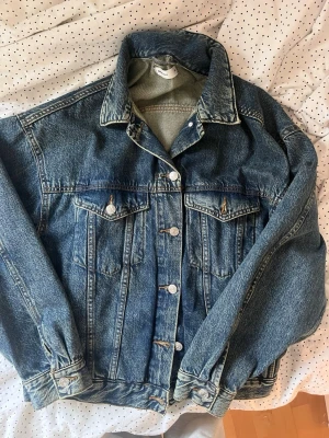 Klassisk blå jeansjacka  - Snygg blå jeansjacka i klassisk modell med raka sömmar, två bröstfickor med lock och knappar framtill. Jackan har en avslappnad passform och tidlös look som passar till det mesta. Perfekt för dig som gillar streetwear eller vintage vibes.
