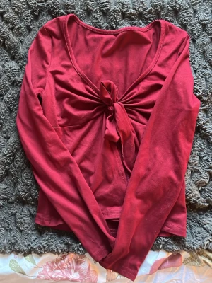Röd långärmad topp med knyt - Trendig röd topp med långa ärmar och snygg knytning framtill. Djup v-ringning ger en modern look och toppen är tillverkad i mjukt bomullsmaterial. Perfekt för dig som vill ha en enkel men ändå iögonfallande stil.