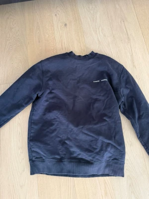 Mörkblå crewneck från Samsoe Samsoe - En stilren mörkblå crewneck från Samsoe Samsoe med liten vit logga på bröstet. Tröjan har rund halsringning, ribbade muddar vid ärmslut och nederkant samt en avslappnad passform. Perfekt till jeans eller sweatpants för en casual look.