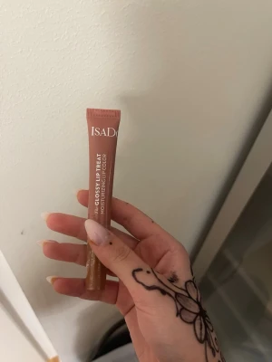 IsaDora Glossy Lip Treat nude - Säljer ett IsaDora Glossy Lip Treat läppglans i en snygg nude-rosa nyans. Tuben är smidig och lätt att ta med i väskan. Ger glansiga och återfuktade läppar med en mjuk finish. Perfekt för dig som gillar naturliga toner och glossig look.