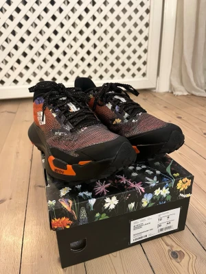The North Face Löparskor - Ett par snygga löparskor från The North Face med svart och orange mesh, detaljer i blommigt mönster med fin sula. Mellansulan består av superkritisk TPU-skum, vilket ger en mjukare och mer responsiv känsla än tidigare versioner. Skorna är ALDRIG använda och är Perfekta för dig som gillar att springa i Terräng, skog och väg!  Nypris går för runt 1749kr på löplabbet. Limited edition‼️‼️