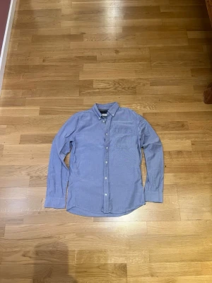 Blå långärmad skjorta från Jack and Jones - Klassisk blå skjorta från Gant med lång ärm och bröstficka. Skjortan har knappar framtill och en stilren krage. Tillverkad i bomull för en bekväm känsla och passar perfekt till både jeans och chinos.