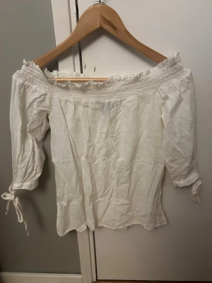 Vit offshoulder topp Atmosphere - Söt vit offshoulder topp från Atmosphere med trekvartsärm och knyt vid ärmsluten. Toppen har en lätt struktur med små prickar i tyget och smock upptill💞