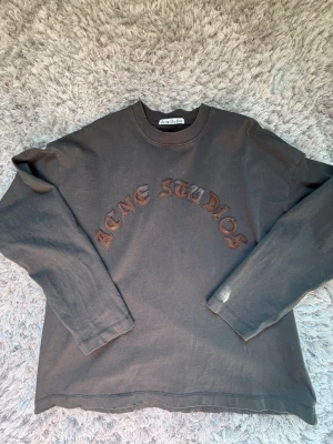 Mörkgrå långärmad topp Acne Studios Storlek S - Säljer en mörkgrå långärmad topp från Acne Studios med broderad logga i brunt framtill. Oversized passform och mjukt bomullsmaterial. Perfekt för en avslappnad och trendig look. Bra skick, sparsamt använd, snygg passform. Rekommenderas starkt. Storlek S, men den kan passa M också!
