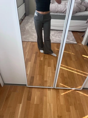 Gråa bootcut kostymbyxor - Säljer ett par gråa bootcut kostymbyxor från ginatricot. Snygg passform som framhäver midjan och ger en trendig siluett. Perfekta till crop tops eller hoodies. Materialet är stretchigt och bekvämt.