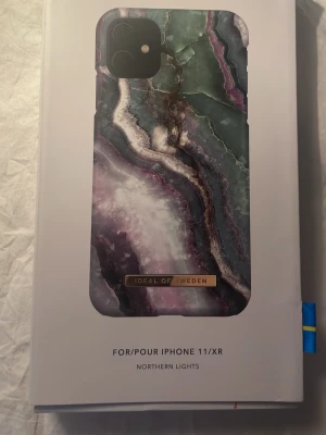 iDeal of Sweden mobilskal Northern Lights - Snyggt mobilskal till iPhone 11/XR från iDeal of Sweden med marmorinspirerat mönster i grönt, lila, vitt och svart. Skalets design heter Northern Lights och har en lyxig känsla med guldfärgad logga. Tillverkat i hårdplast som skyddar mobilen mot repor.
