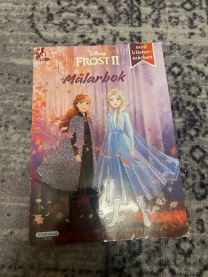 Frost II Målarbok med klistermärken - Målarbok med motiv från Disney Frost II. Omslaget är färgglatt med Anna och Elsa i glittriga kläder och höstlöv i bakgrunden. Innehåller sidor att färglägga samt klistermärken. Perfekt för dig som gillar kreativa aktiviteter och Frost.