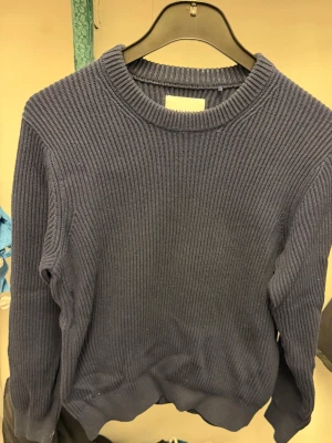 Mörkblå ribbstickad tröja - Snygg mörkblå stickad tröja med ribbad struktur och rund hals. Tröjan har långa ärmar och en klassisk passform som funkar till det mesta. Perfekt för dig som gillar enkel men stilren design.