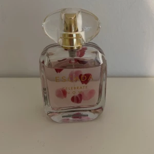 Escada Celebrate N.O.W. parfym - Escada Celebrate N.O.W. parfym i en elegant glasflaska med gulddetaljer och genomskinligt lock. Flaskan har rosa detaljer inuti och text i guld på framsidan. Perfekt för dig som gillar fräscha och feminina dofter.