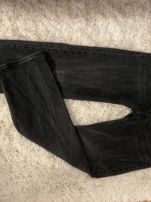 Svarta raka jeans - Säljer ett par svarta jeans med rak passform och diskret tvättad look. Jeansen har klassisk femficksdesign och är tillverkade i denim. Perfekta för dig som gillar en enkel och stilren stil.