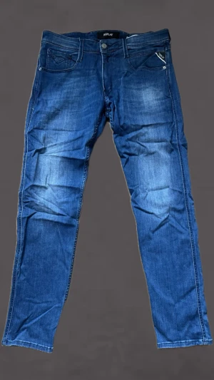 Blå jeans från Replay - Snygga blå jeans från Replay med klassisk femficksmodell och raka ben. Jeansen har en lätt tvättad look och detaljerade sömmar på bakfickorna. Tillverkade i mjukt denimtyg som ger en bekväm passform. Perfekta för en avslappnad stil. De har inte blivit använda på ett tag därav ej så släta😁👊