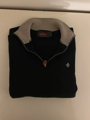 Mörkblå stickad tröja från Morris - Snygg mörkblå stickad tröja från Morris med halv dragkedja och kontrasterande ljusgrå krage. Tröjan har lång ärm, ribbade muddar och en liten broderad logga på bröstet. Perfekt för lager på lager och stilren look. Mycket fint skick. Köpt för 1500. Storlek S men passar XS👍