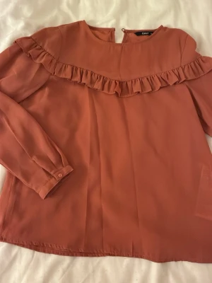 Smutsrosa blus med volang från ONLY - Supersnygg smutsrosa blus från ONLY med lång ärm och volangdetalj över bröstet.