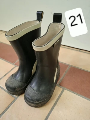 Svarta gummistövlar med vit kant - Säljer ett par klassiska svarta gummistövlar från Viking med vit kant upptill och praktiska dragflikar. Stövlarna har förstärkt tå och sula i grovt mönster för extra grepp. Perfekta för regniga dagar och leriga äventyr.