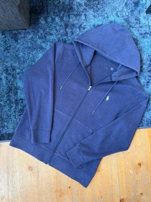 Marinblå Ralph Lauren Hoodie - Hej!👋  Säljer en marinblå zip up hoodie från Polo Ralph Lauren. Hoodien har inga fläckar eller hål, men är lite nopprig i tyget efter användning. Utöver detta så är den i mycket fint skick. Storleken har suddats ut i tvättmaskinen, men den sitter som en M. Skicka gärna mått på begäran. Hör av er vid frågor  Skickar snabbt!🚛📦