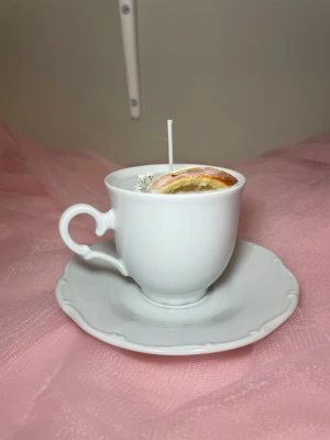 Doftljus i vaniljdoft i en vit tekopp med fat - Det här ljuset är gjort av återanvändbara material. Tekoppen är köpt secondhand och stearinet är från kyrkor som tänkte slänga det. Det här ljuset har en svag doft utav vanilj, så känsliga även kan använda det. Det här ljuset har även torkade blommor och apelsin på som dekoration. 