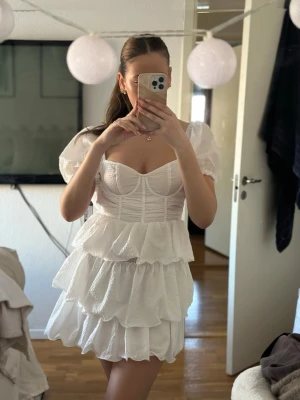 Vit volangklänning PrettyLittleThing - Supersöt vit kort klänning från PrettyLittleThing med puffärmar, volanger i flera lager och markerad byst. Klänningen har en feminin siluett och är perfekt för sommarens alla tillfällen. Tillverkad i lätt och luftig polyester.