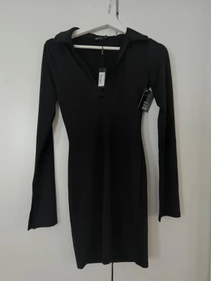 Svart långärmad klänning nelly - Stilren svart klänning från nelly med lång ärm och v-ringning. Klänningen har en kroppsnära passform och är tillverkad i ett mjukt, stretchigt material. 