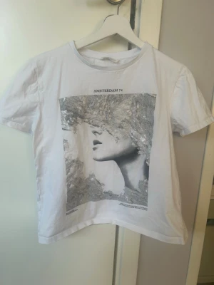Vit t-shirt med tryck från Zara💕💕 - Säljer en vit t-shirt från Zara med ett stort konstnärligt tryck i silver och grått på framsidan och texten 'AMSTERDAM 74' ovanför motivet.💕💕💕💕 T-shirten har rund hals och korta ärmar, perfekt för en trendig och avslappnad stil.💕💕💕I bra skick💕💕Jag säljer den för 60 kr💕💕Hör av er vid intresse💕💕💕💕💕
