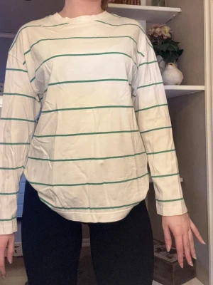 Vit randig långärmad tröja Gina Tricot - Vit långärmad tröja från Gina Tricot med gröna ränder. Enkel och clean design med rund halsringning och relaxed fit. Perfekt för dig som gillar en stilren och chill vibe. Tillverkad i mjuk bomull för skön känsla hela dagen.