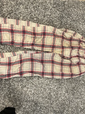 Rutiga pyjamasbyxor i bomull - Ett par klassiska pyjamasbyxor i mjuk bomull med rutigt mönster i vitt, rött och blått. Byxorna har resår i midjan för extra komfort och en avslappnad passform. Perfekta för mysiga hemmakvällar.