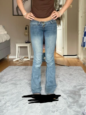 Blå bootcut jeans med låg midja - Säljer ett par ljusblå bootcut jeans med låg midja och klassisk femficksmodell. Jeansen har en snygg tvättad look och är perfekta för dig som gillar retrostil. Materialet är denim med lätt stretch för skön passform. Passar perfekt till crop tops och sneakers.